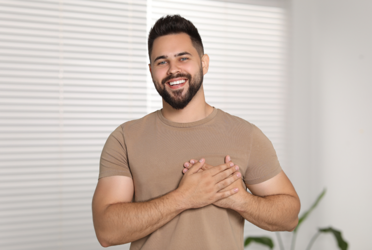 Happy Grateful Man Holding Hands near Heart Indoors