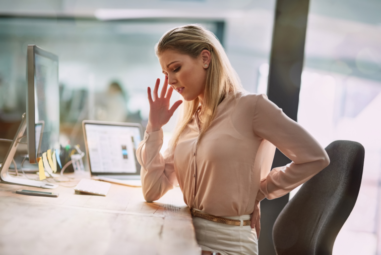 A young business woman suffering from backpain sitting at her desk; ergonomic posture, occupational therapy